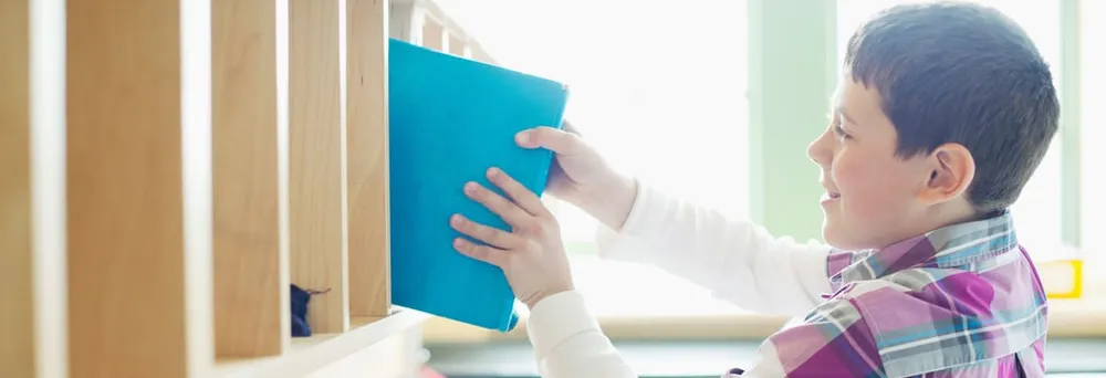 Junge stellt etikettierten Ordner ins Schulregal 