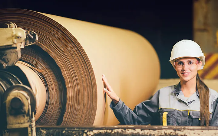 Frau steht neben Testlinerpapier-Rolle Frau steht neben Testlinerpapier-Rolle