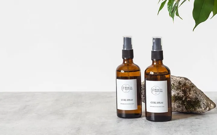 Amber spray bottles with minimalist white labels on a stone surface