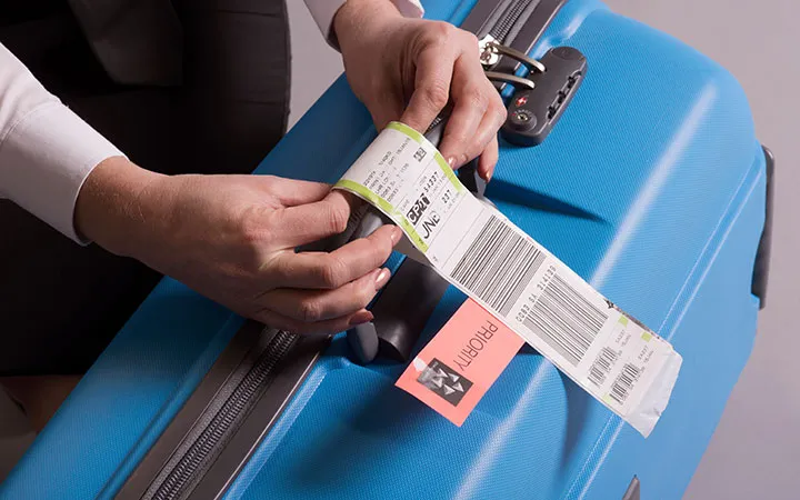 Frau bringt Etikett an Koffer an Frau bringt Etikett an Koffer an