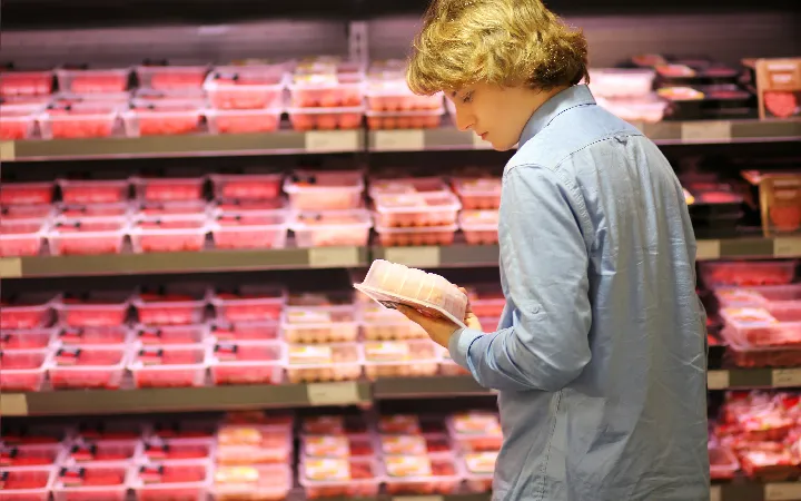 Mann liest in der Fleischabteilung das Rückseitenetikett auf einer Fleischverpackung durch Mann liest in der Fleischabteilung das Rückseitenetikett auf einer Fleischverpackung durch